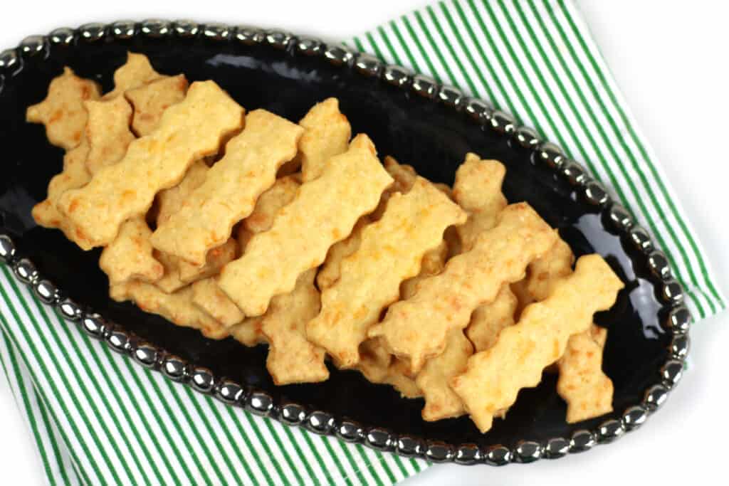 A black platter with cheese straws on top of a green napkin.