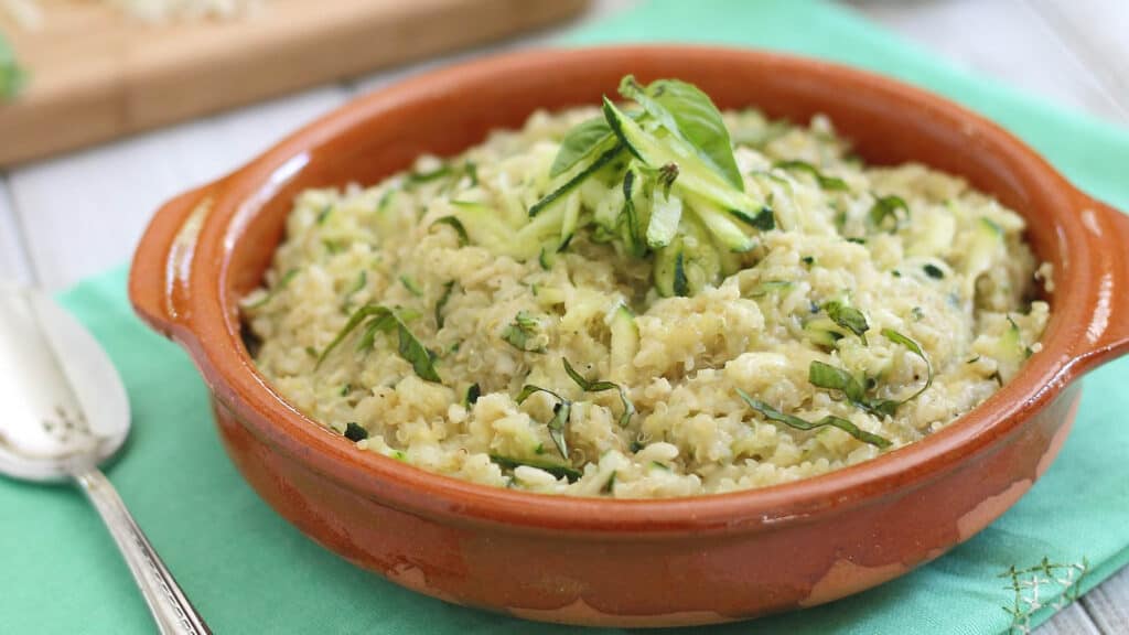 Cheesy zucchini quinoa in a terracotta bowl topped with basil.