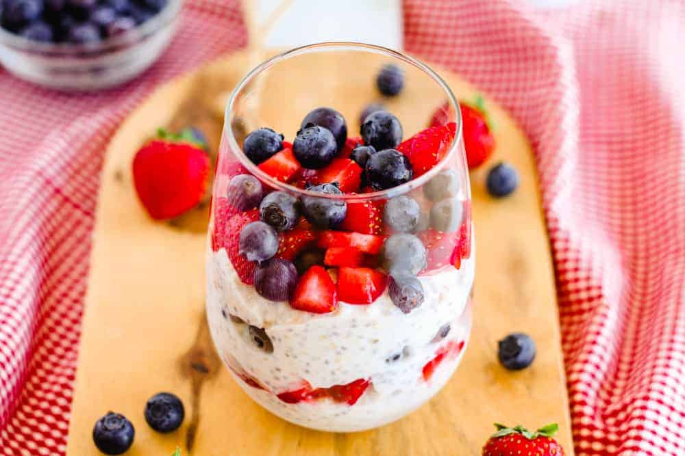 A glass with chia overnight oats garnished with strawberries and blueberries.