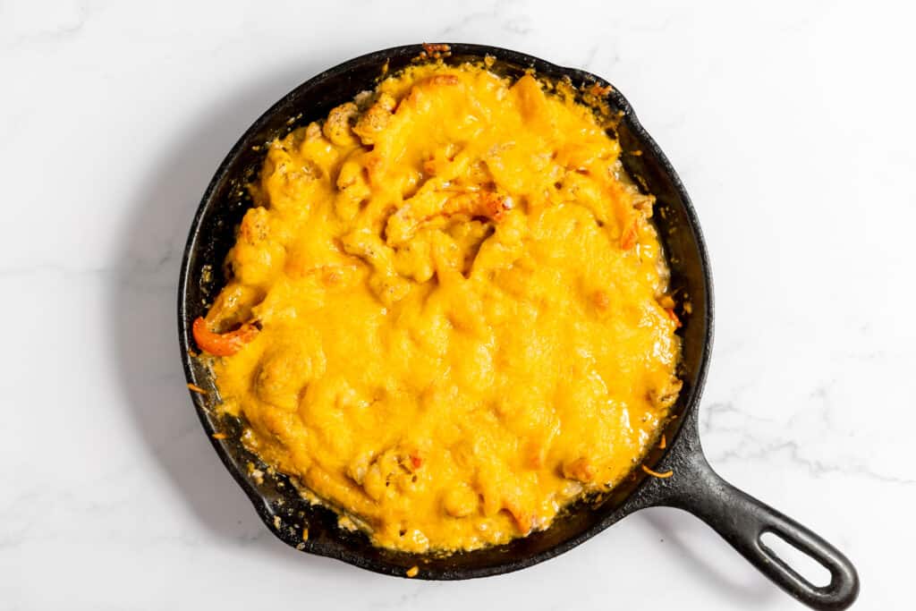 A cast iron skillet filled with baked macaroni and cheese, topped with gooey, melted golden cheddar cheese that will leave you begging for more.