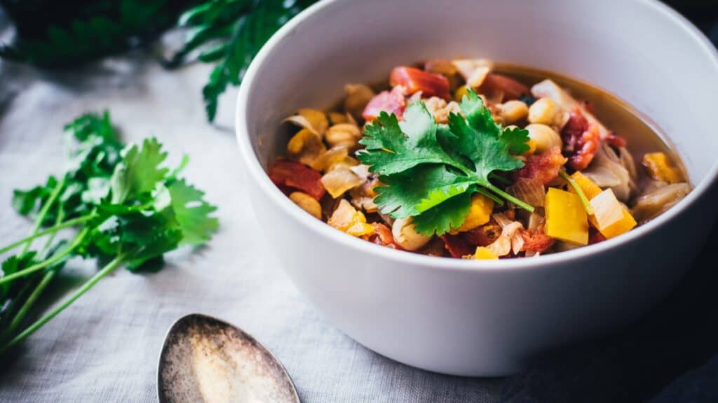 A white bowl filled with a colorful chili garnished with green herbs.