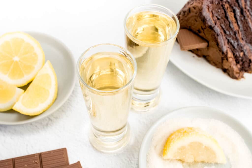 A slice of chocolate cake next to two chocolate cake shots and lemon wedges.