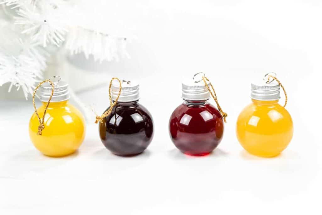 Round ball ornaments filled with juices next to a white Christmas tree.