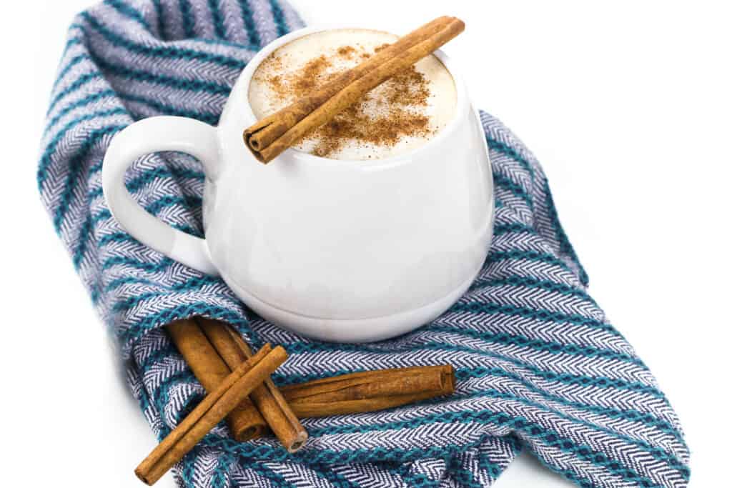A latte in a grey mug with a cinnamon stick on top, on top of a blue kitchen towel.