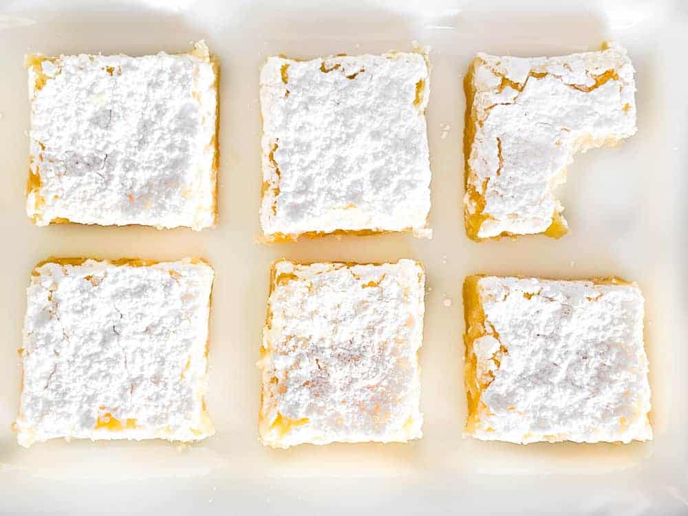 Lemon bars on a plate, one has a bite take out of it. 