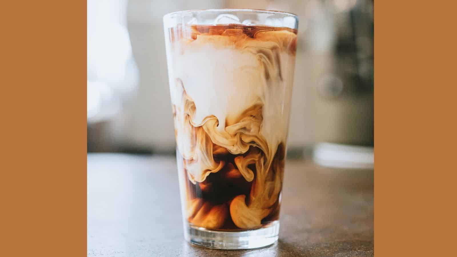 A picture of cold brew coffee over ice with milk swirling in glass.