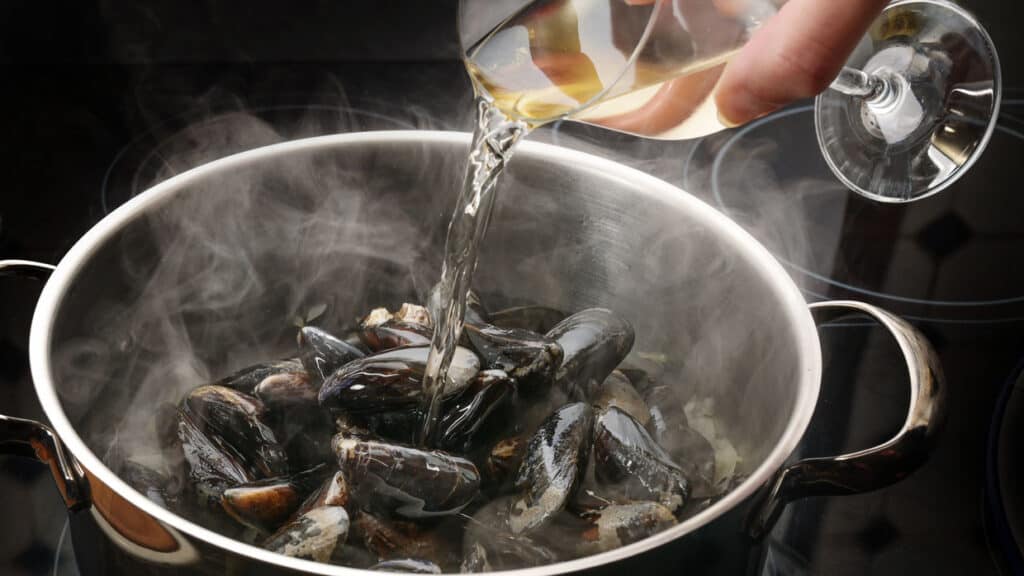 Steaming mussels in a pot are deglazed with white wine, cooking concept for a delicious seafood dish.