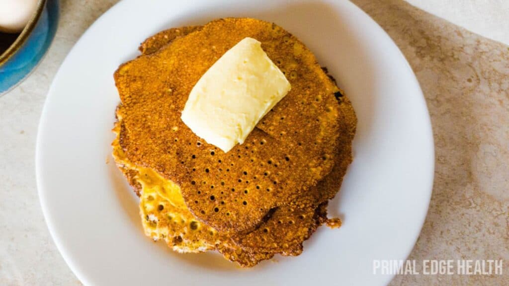 A stack of cream cheese pancakes on white plate with butter.