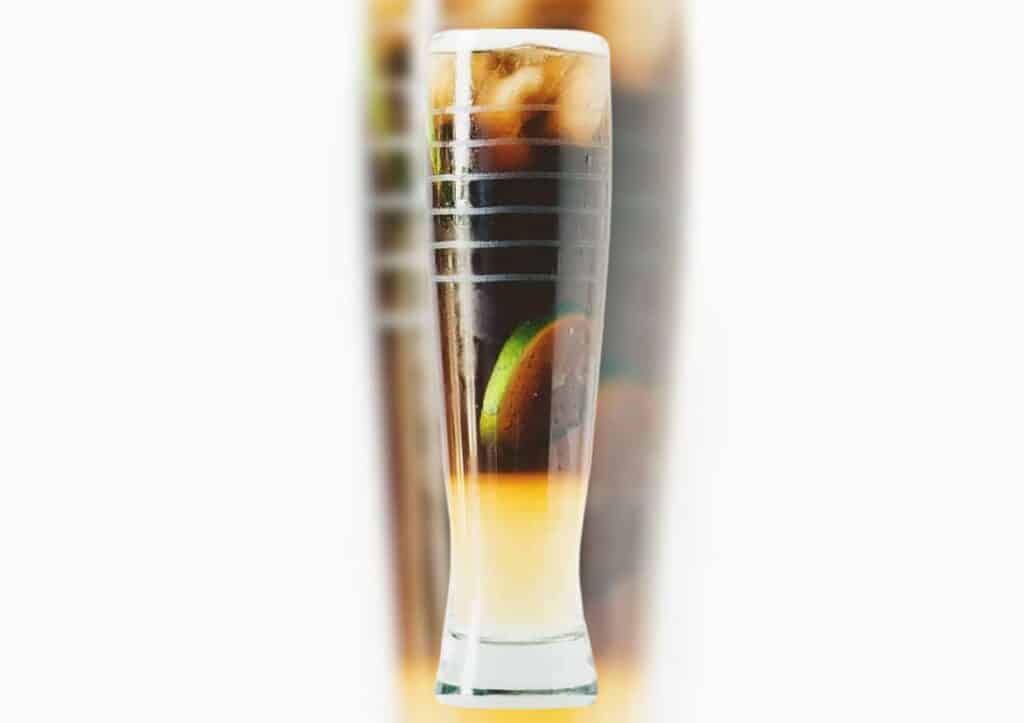 Cuba libre cocktail in a tall glass with lime wedge.