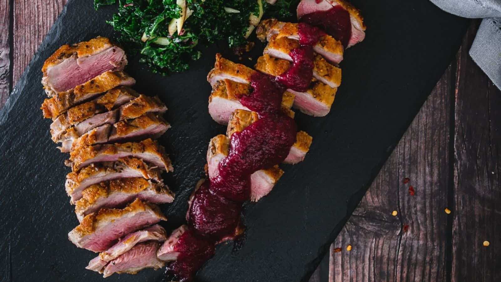 Overhead view of sliced duck breast with berry sauce.