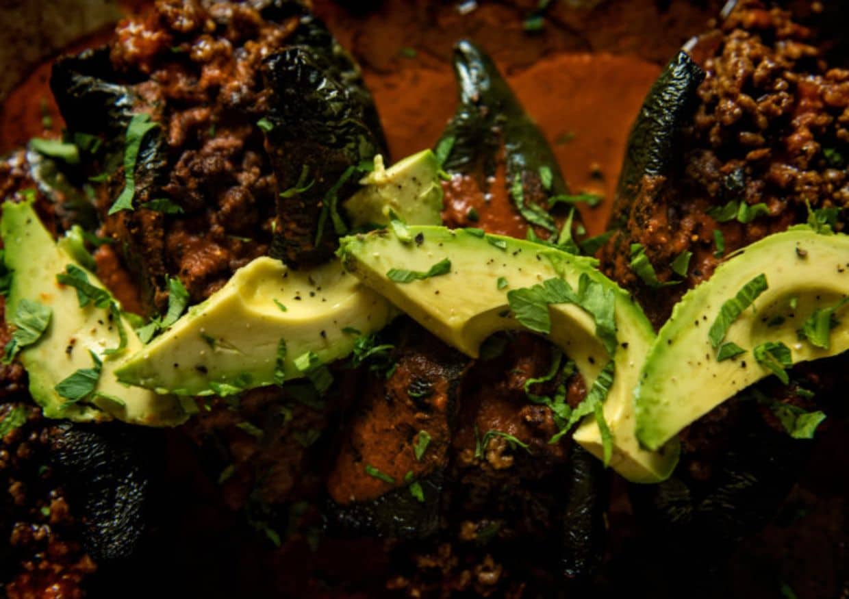 Overhead of avocado slices atop stuffed peppers. 