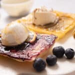 Puff pastry fruit tarts with apples and blueberries on a white board.