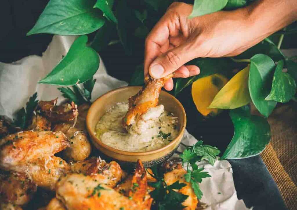 Hand dipping chicken wing in sauce.