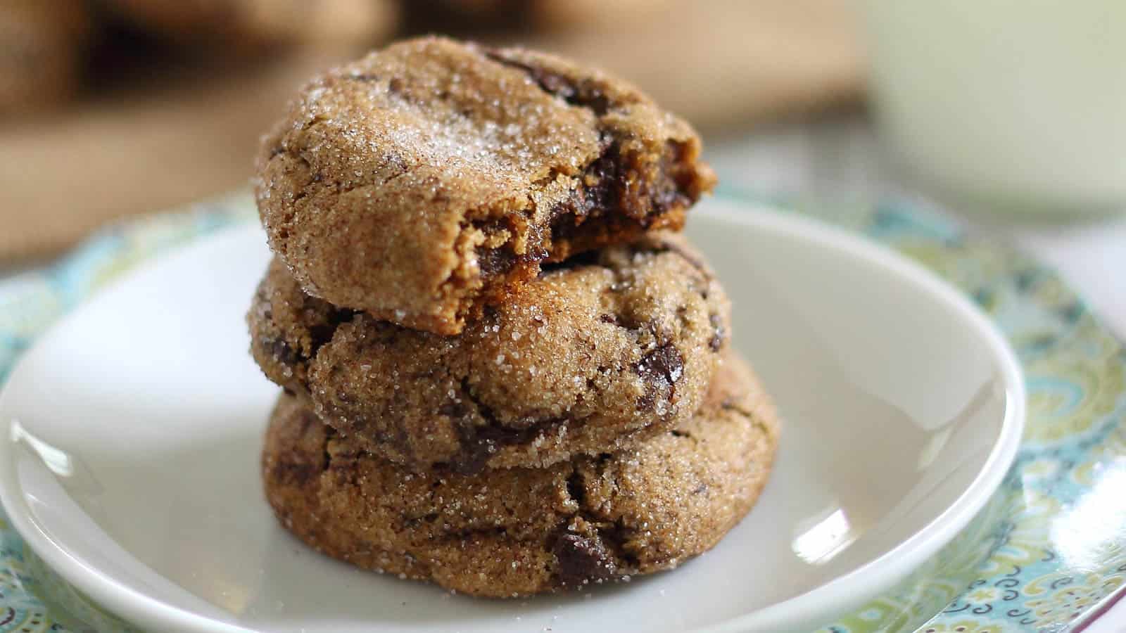 Three gingerbread molasses chocolate chunk cookies stacked on a white plate coated in sugar.