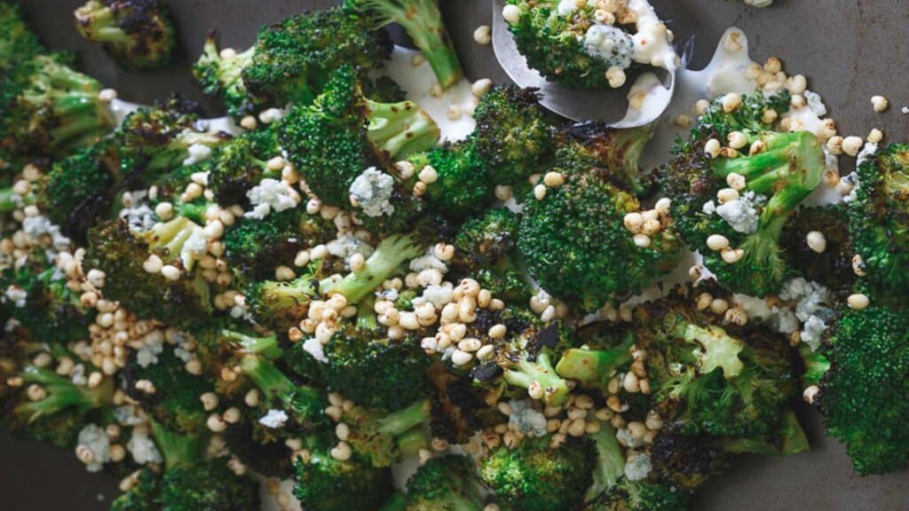 Grilled broccoli on a sheet pan with cheese sauce and crispy puffs.