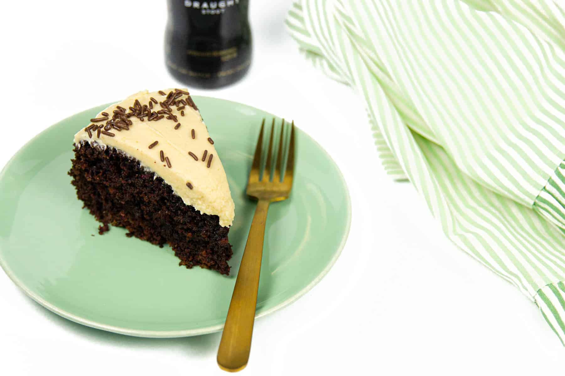 A slice of Chocolate Guinness Cake with a gold fork and a striped kitchen towel.