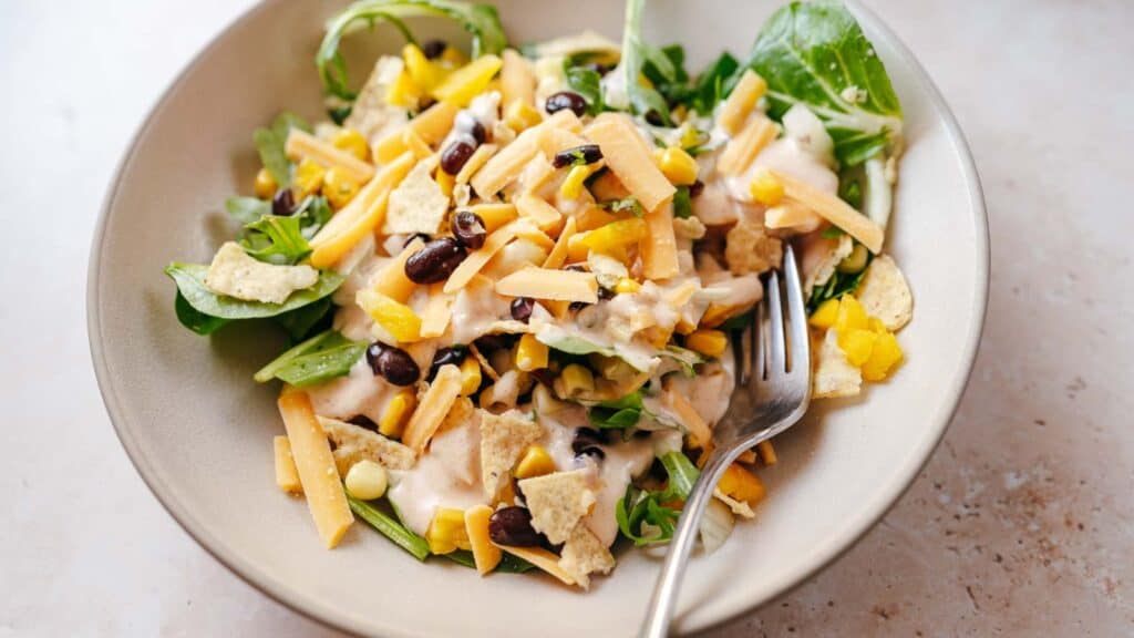 A large tan ceramic bowl filled with salad ingredients and a creamy dressing.