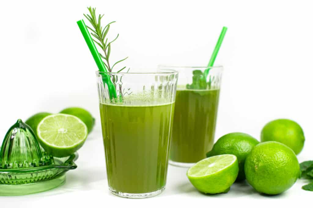 Two glasses of herbal limeade with green straws and limes.