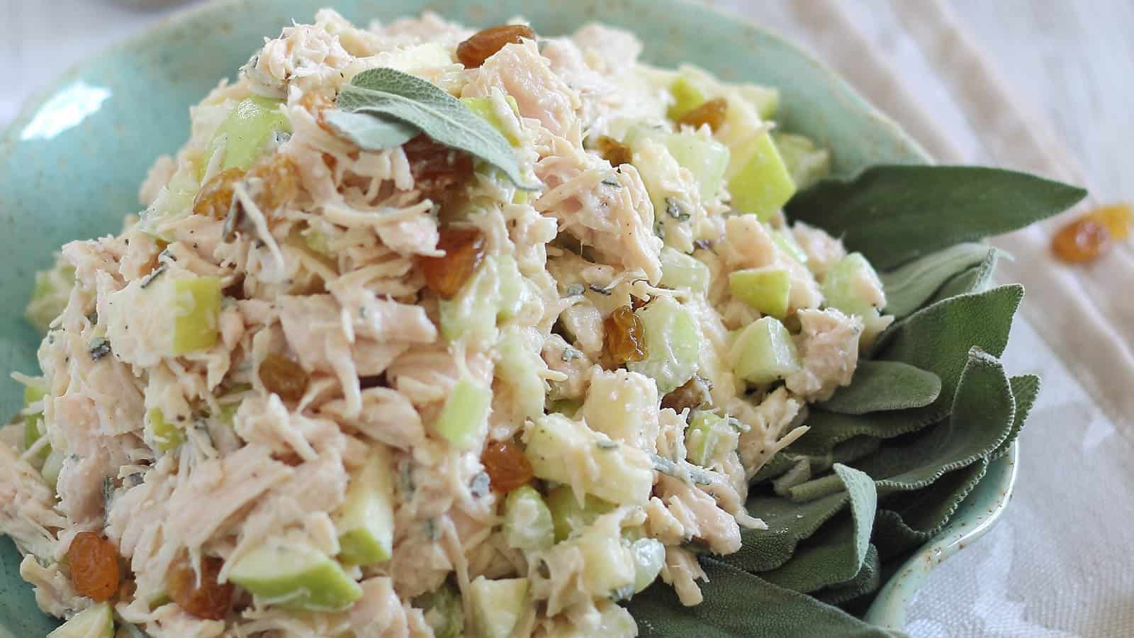 Honey apple chicken salad with fresh sage leaves in a teal bowl.
