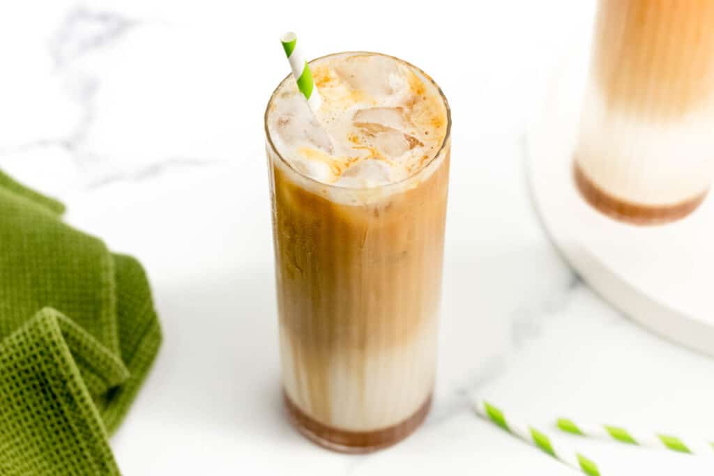 An Iced Caramel Macchiato on a white surface next to a green dish towel.