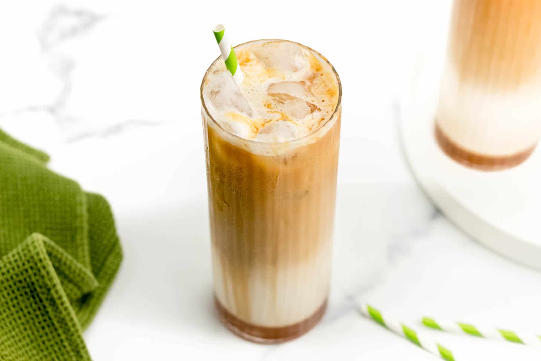 An Iced Caramel Macchiato on a white surface next to a green dish towel.