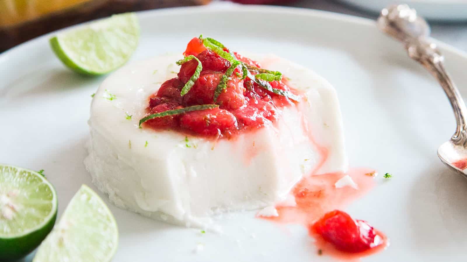 Key lime coconut panna cotta on a white plate topped with a strawberry lime compote.