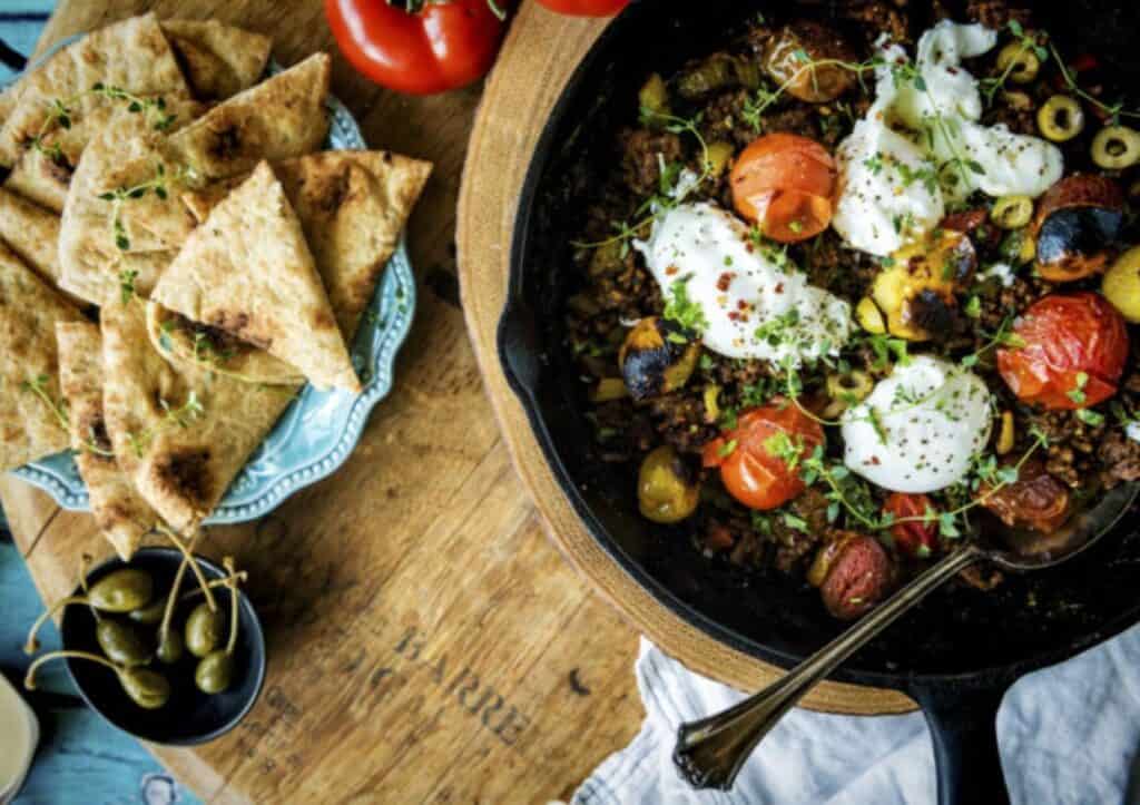 overhead of skillet of poached eggs and ground lamb on platter.