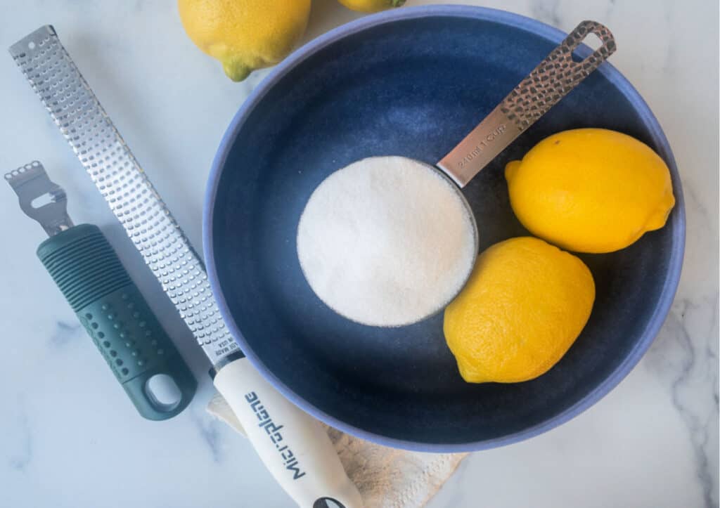 A blue bowl with lemons and sugar, and citrus zesting tools.