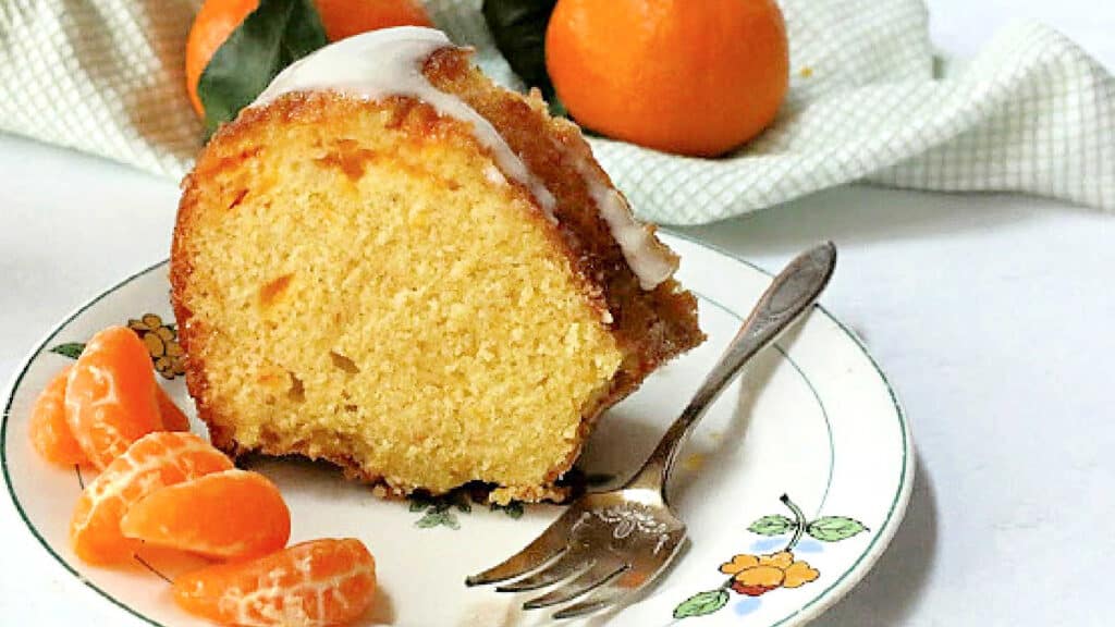 Mandarin Orange Bundt Cake slice on a white plate with slices of oranges.