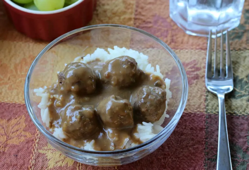 Small glass bowl of meatballs and gravy over rice with a fork beside it.