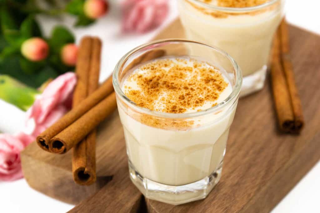 Cinnamon sticks and milk tart shooters on a wooden serving tray.