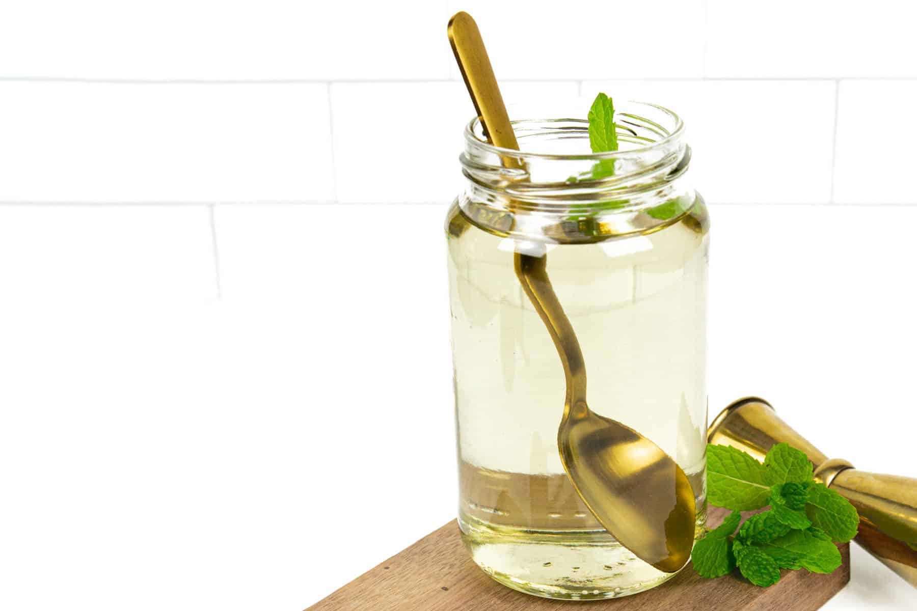 A jar of mint simple syrup with a gold spoon in it.
