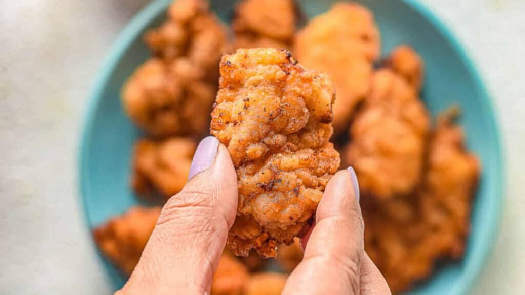 A hand holding a crispy piece of mochiko chicken.