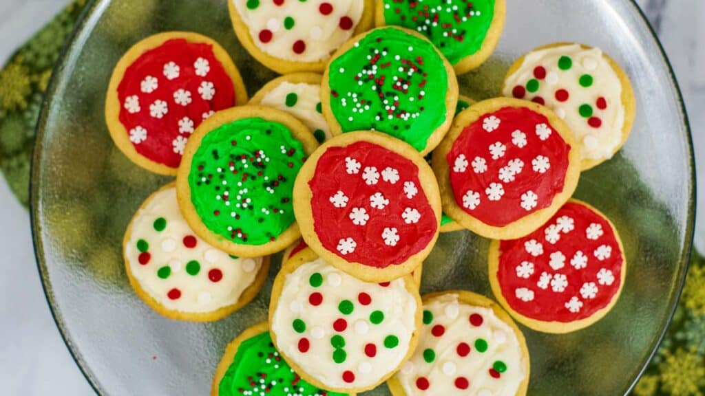 Frosted sugar cookies on a plate decorated with sprinkles.
