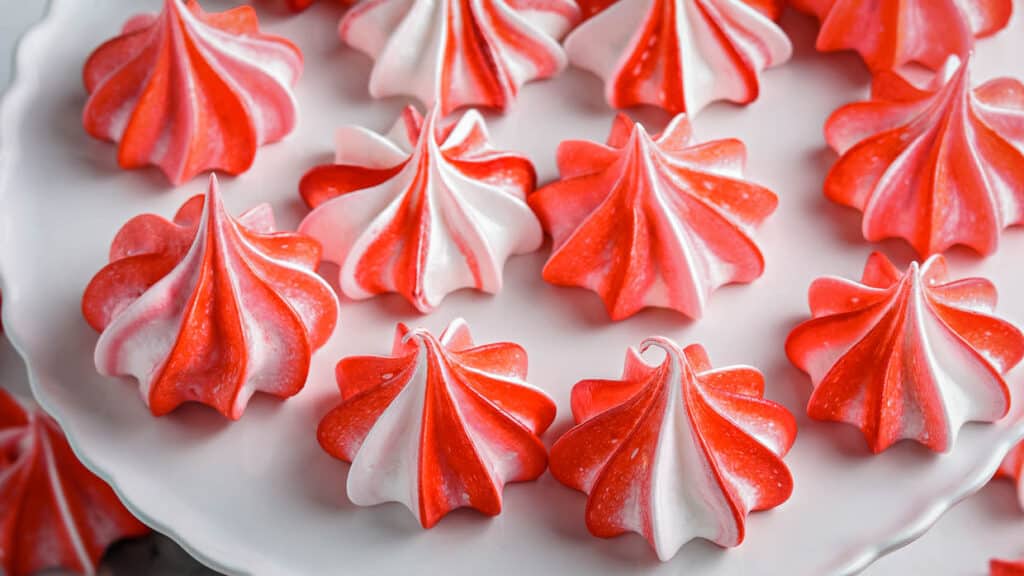 Meringue cookies decorated with red and white stripes on a cake stand.