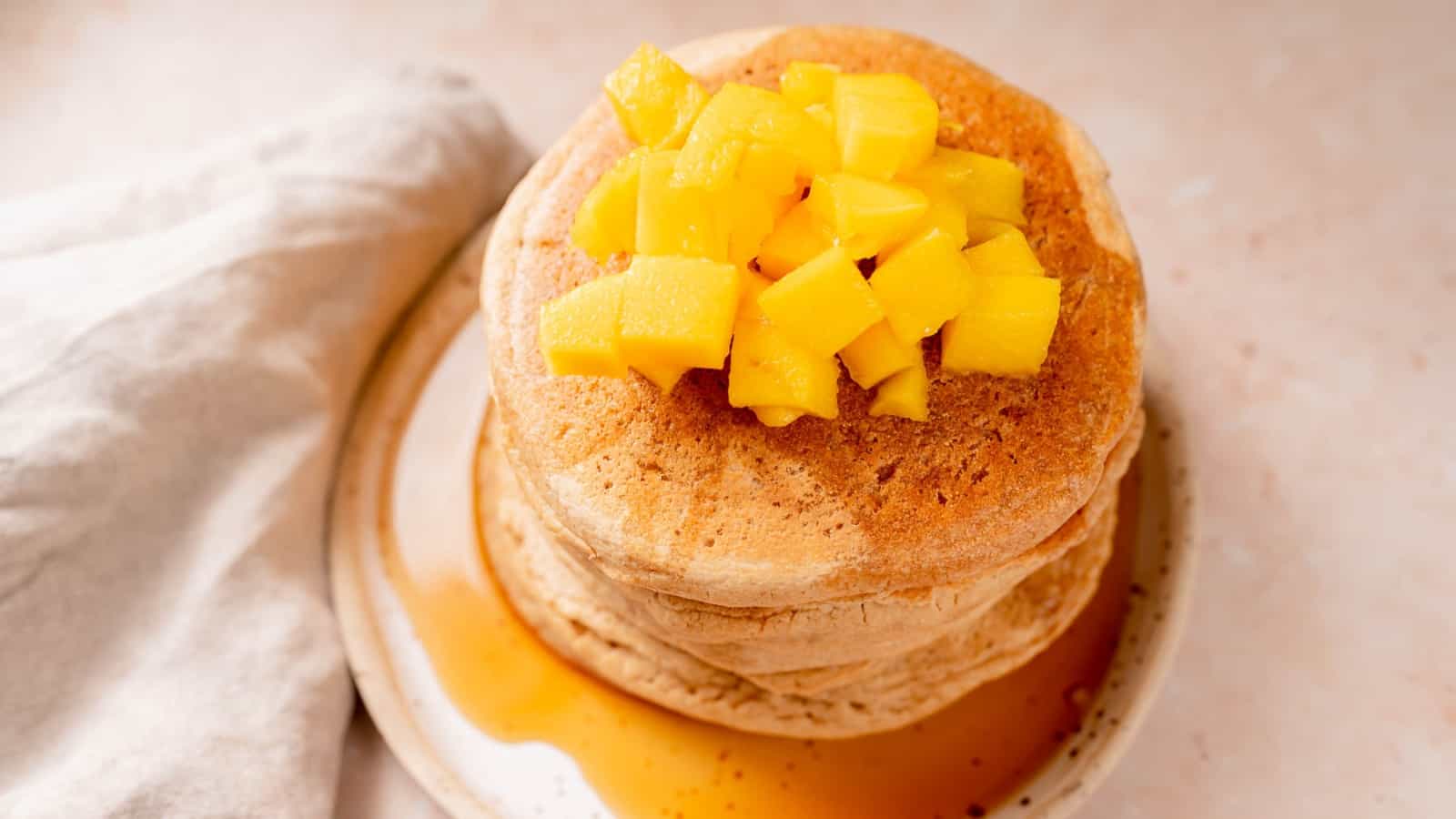 A stack of pancakes topped with fresh mango and maple syrup.