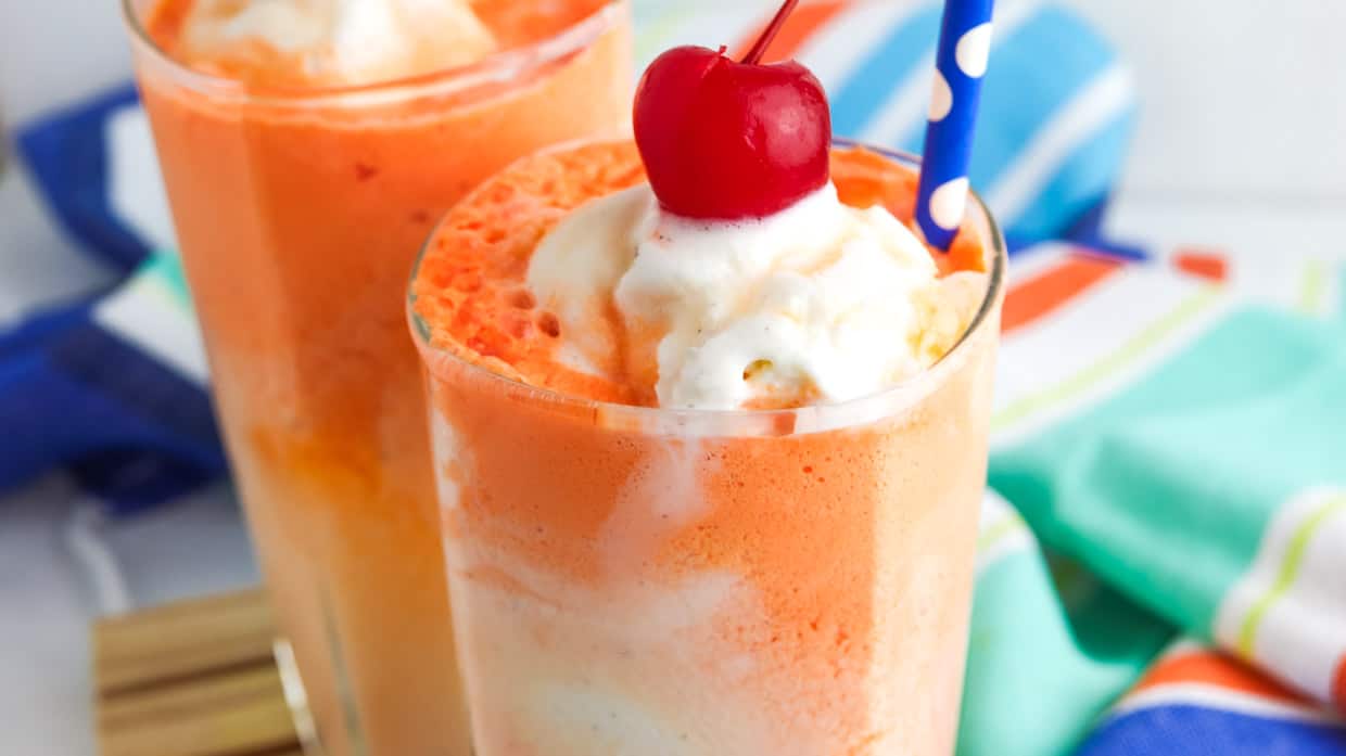 Orange float in a glass topped with whipped cream and a cherry.
