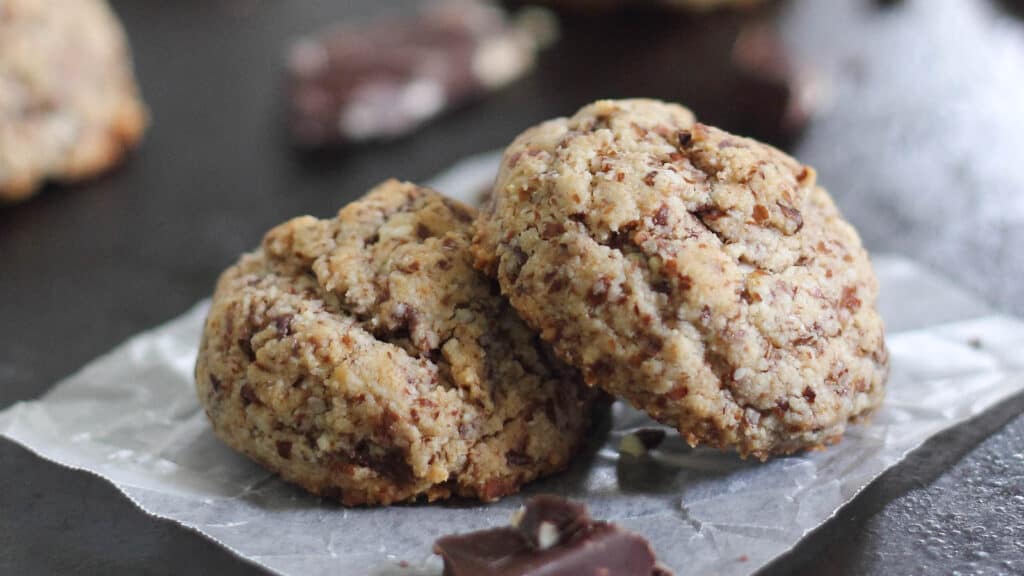 Paleo chocolate chunk cookies sitting on parchment paper with piece of chocolate next to them.