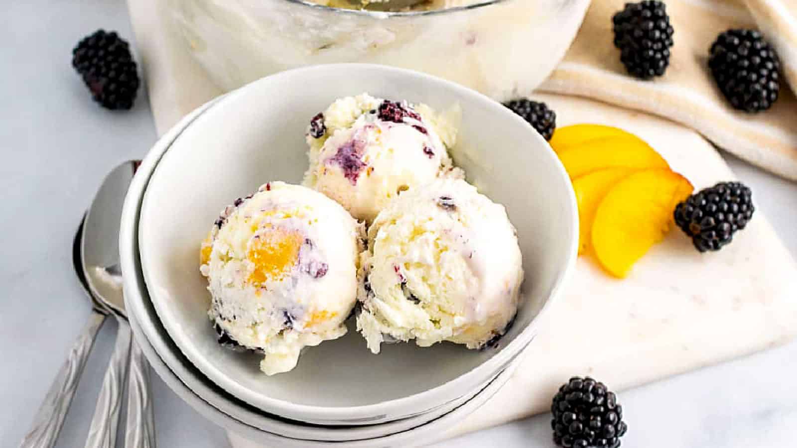 Peach and blackberry ice cream scoops in white bowls.