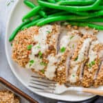 Pecan crusted chicken cut into slices on a plate with honey dijon sauce and green beans.