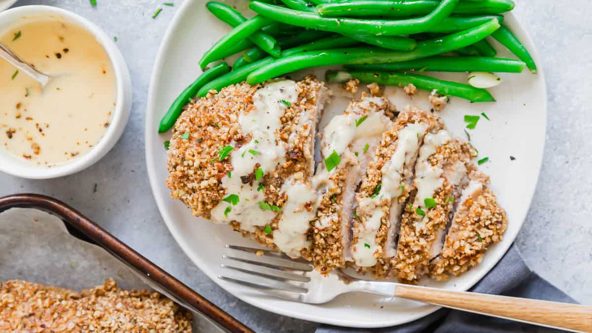 Pecan crusted chicken cut into slices on a plate with honey dijon sauce and green beans.