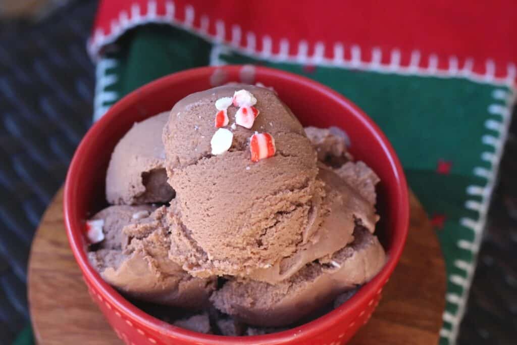 Bowl of ice cream in a red bowl with crushed peppermint topping.