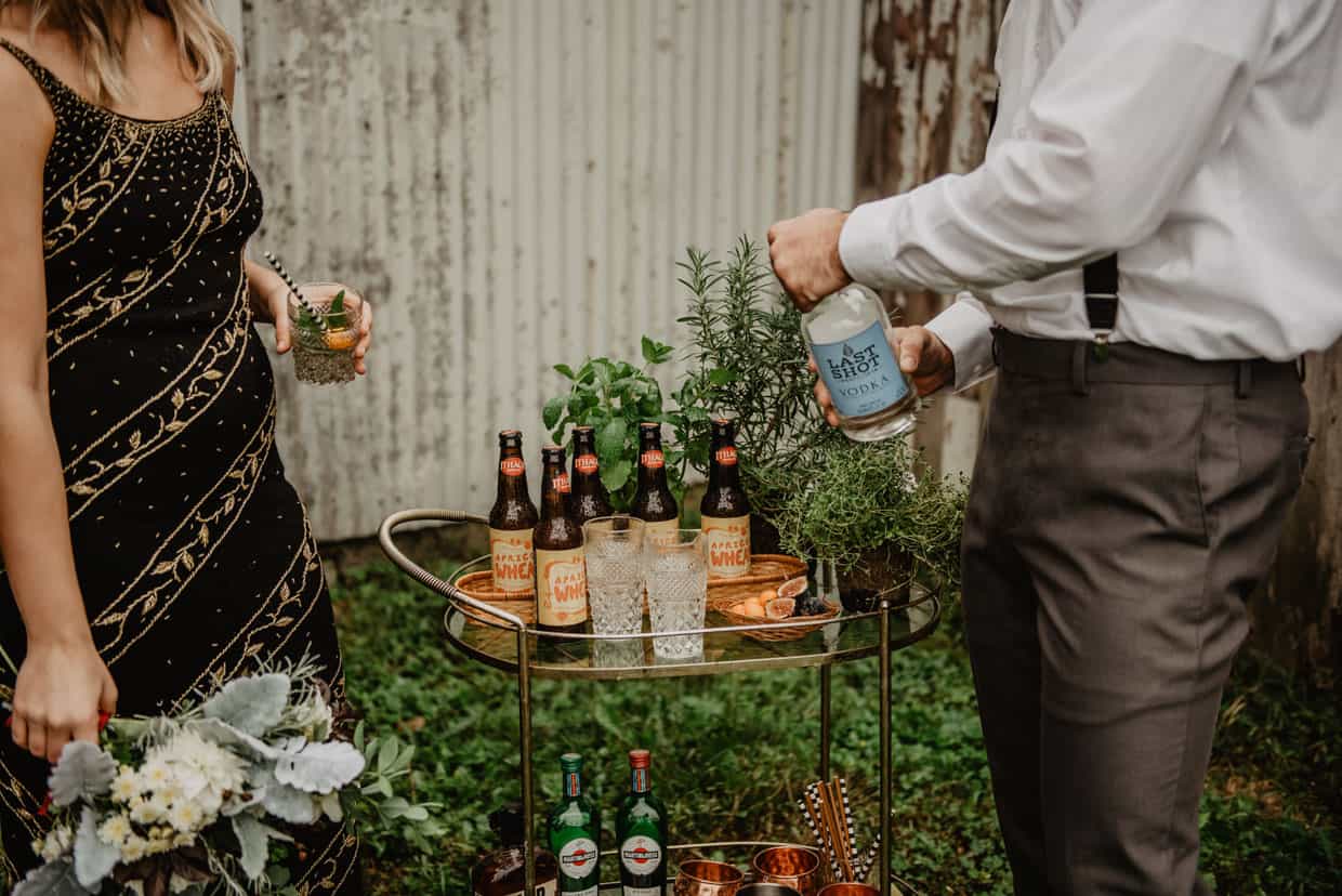 A woman and a man prepare drinks at a bar cart in a backyard.