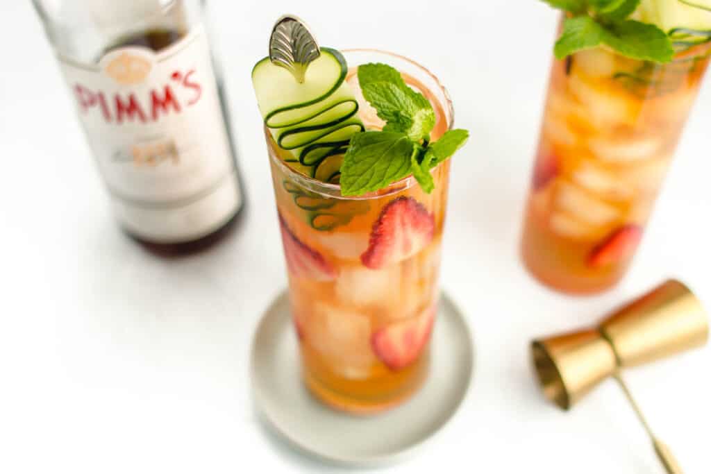 A bottle of Pimms liqueur sits next to two cocktails.