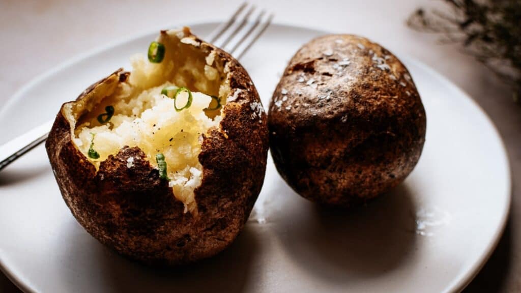 Two baked potatoes resting on a white ceramic plate.