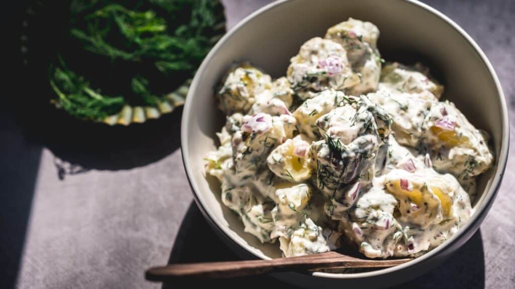A white bowl filled with potato salad, lit by the sun.