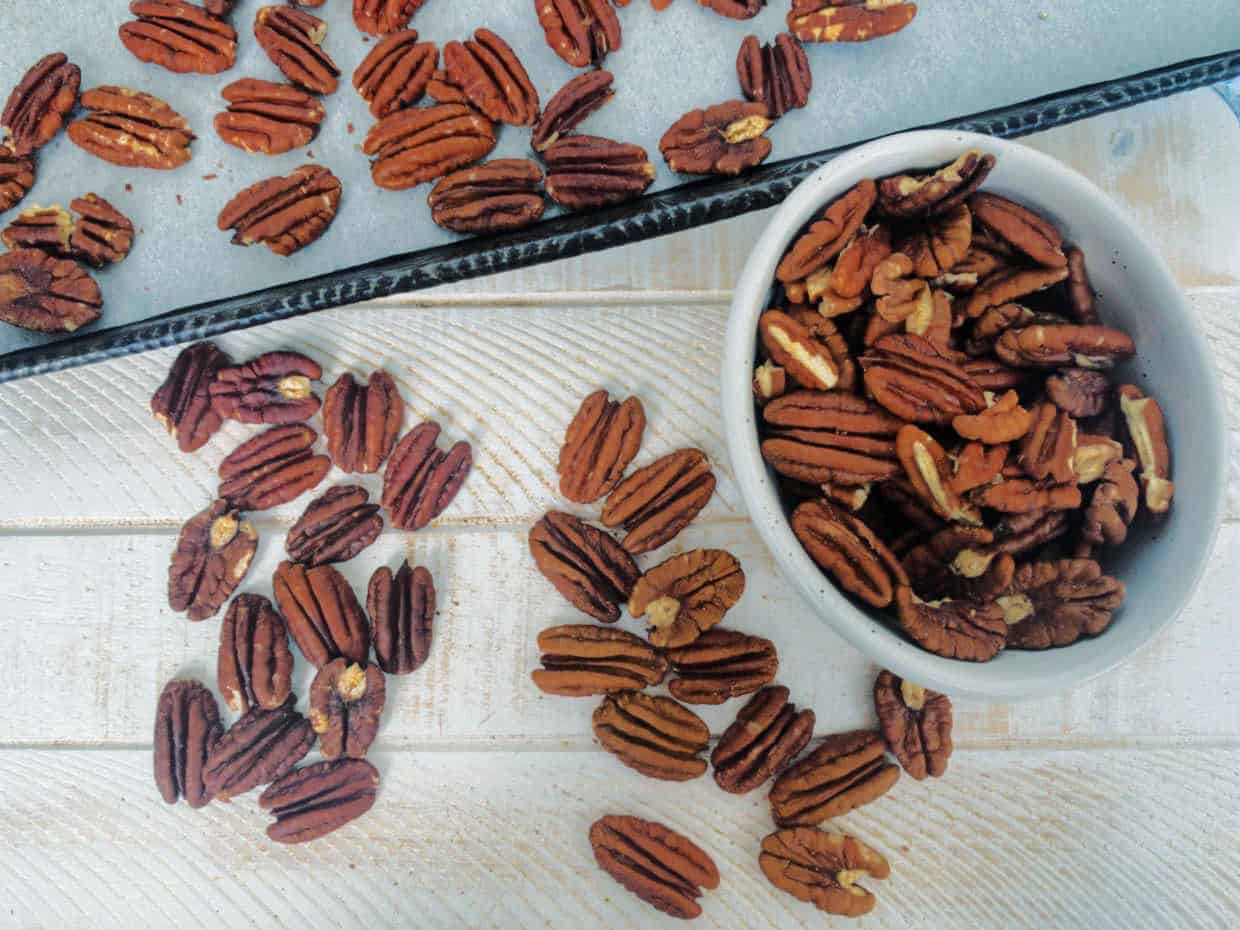 Toasted pecans on a white board on baking sheet.