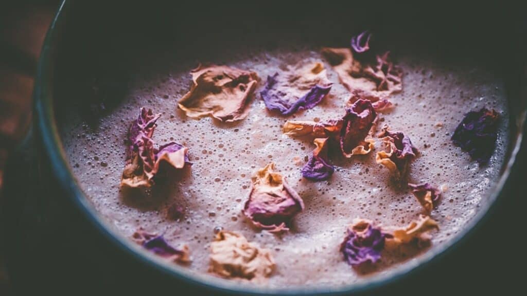 A close shot of a pink frothy beverage garnished with dried rose petals.