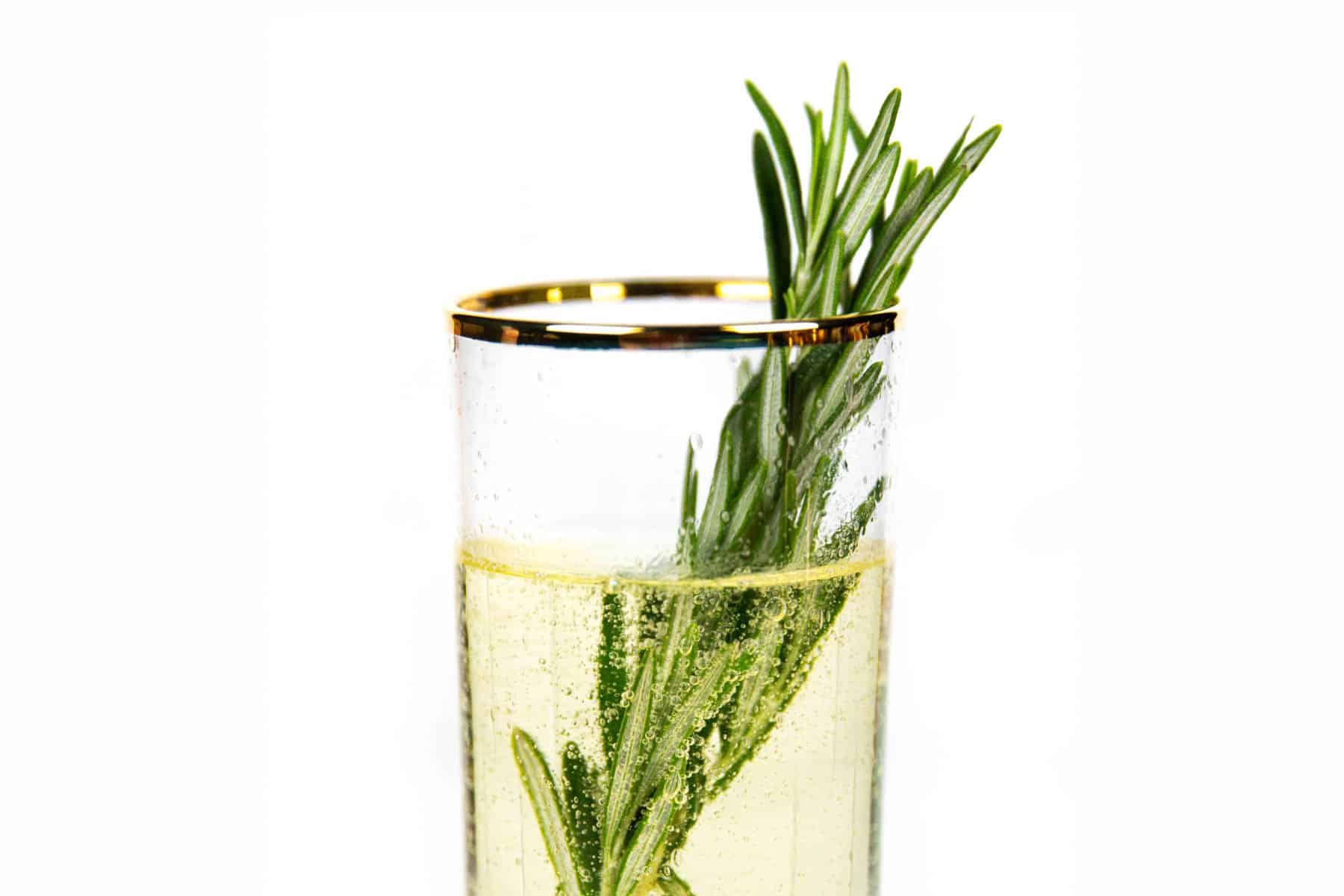 Rosemary sprigs stick out of a gold-rimmed glass with a bubbly cocktail inside.
