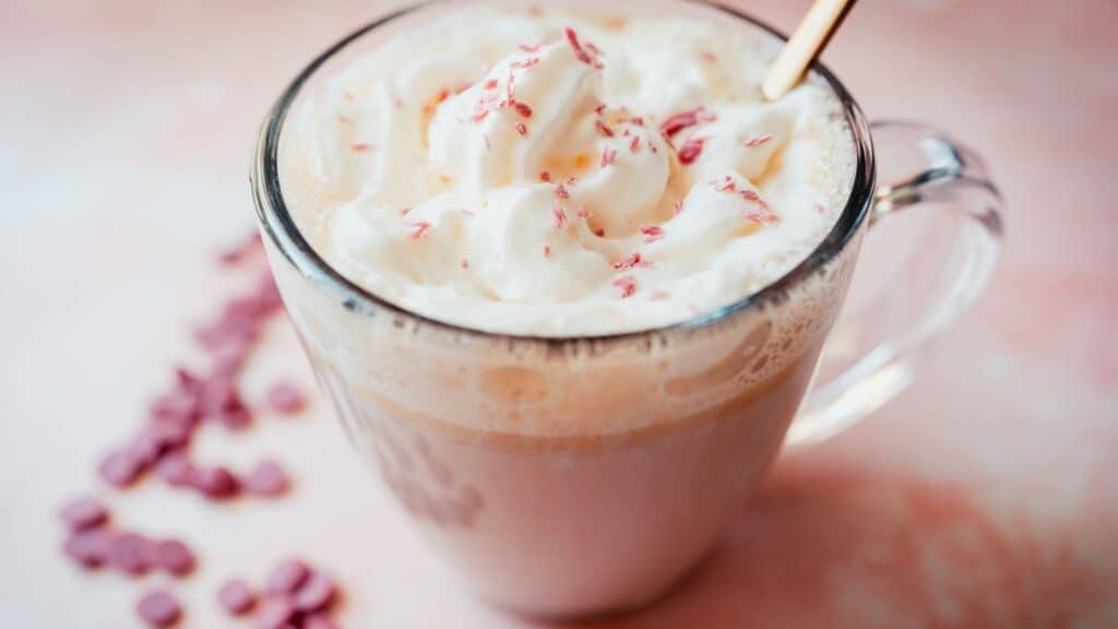 A clear glass mug filled with a pink liquid topped with whipped cream.